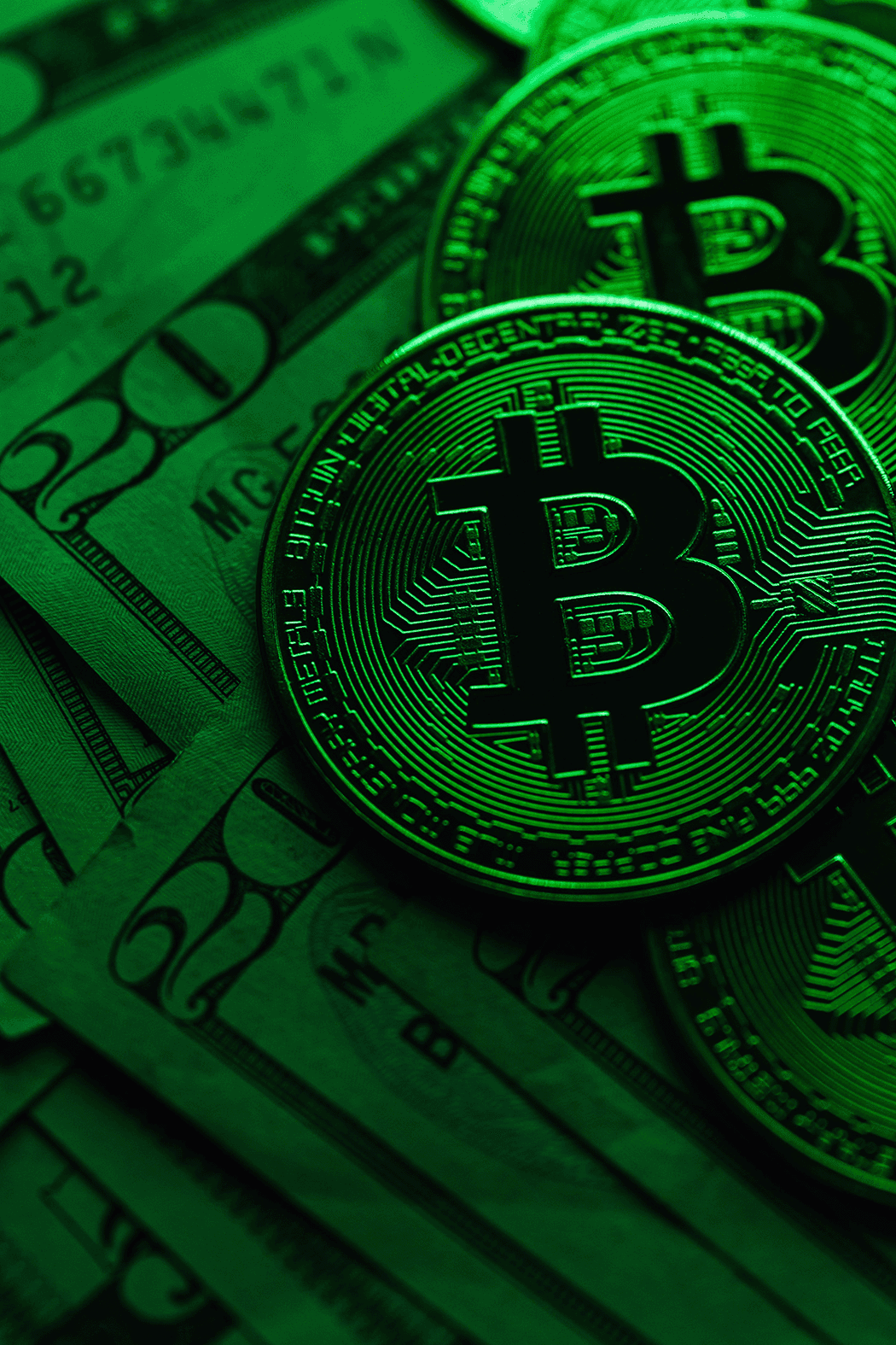 Green-tinted image of Bitcoin coins placed on top of U.S. dollar bills.