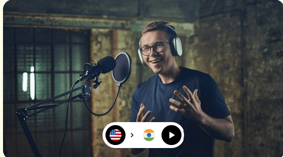 Man in headphones using a microphone in a recording studio with flags of USA and India below.