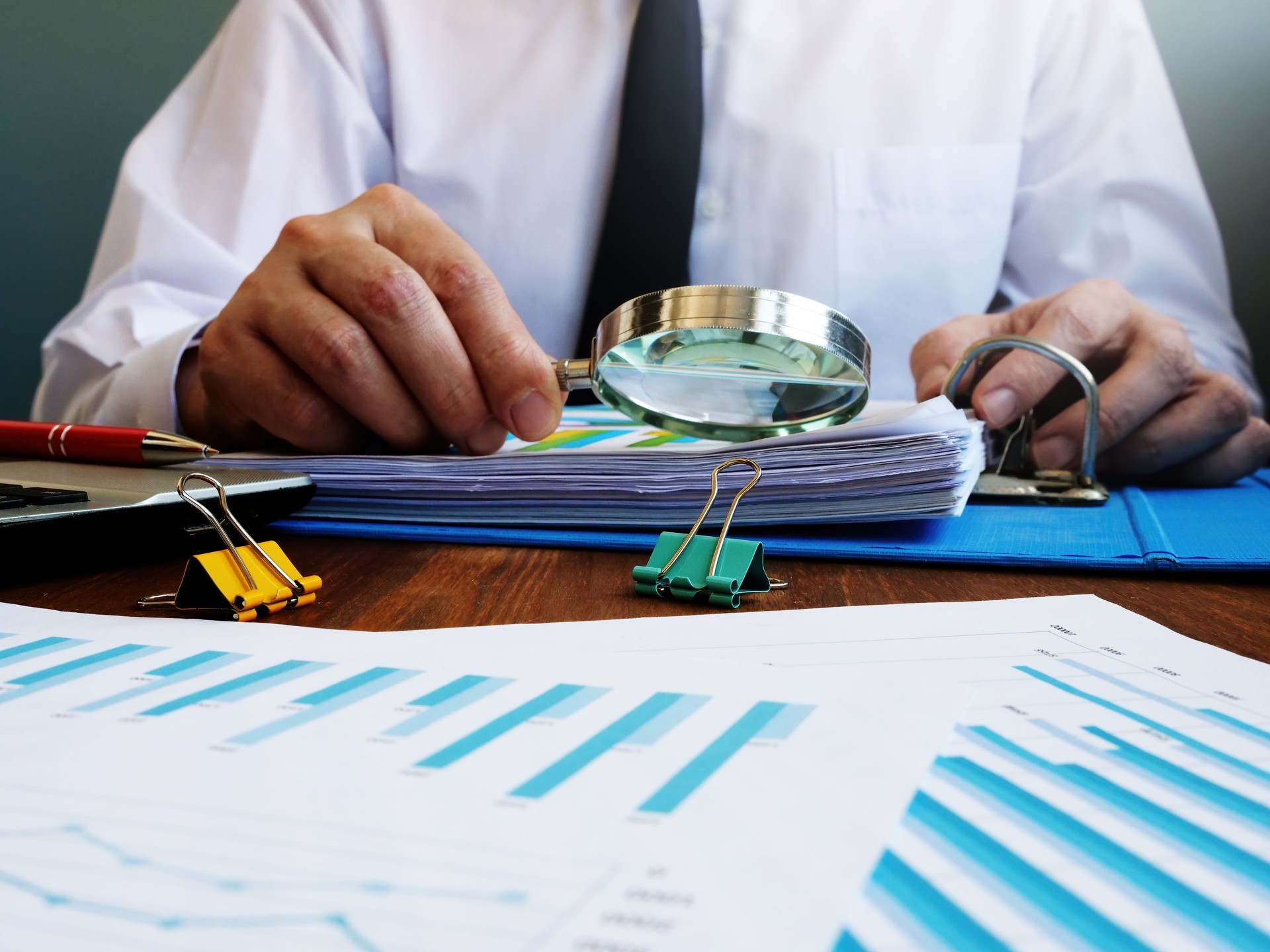 Auditor makes internal audit of company and checks financial report with magnifying glass.