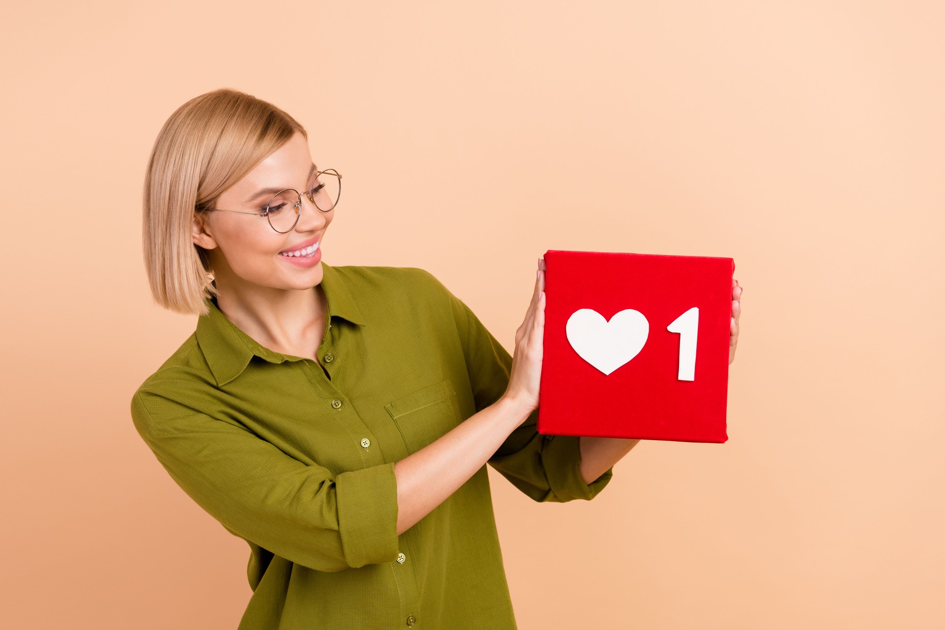 Portrait of cute pleasant girl wear khaki shirt in eyewear look at one social media heart in hands isolated on pastel color background